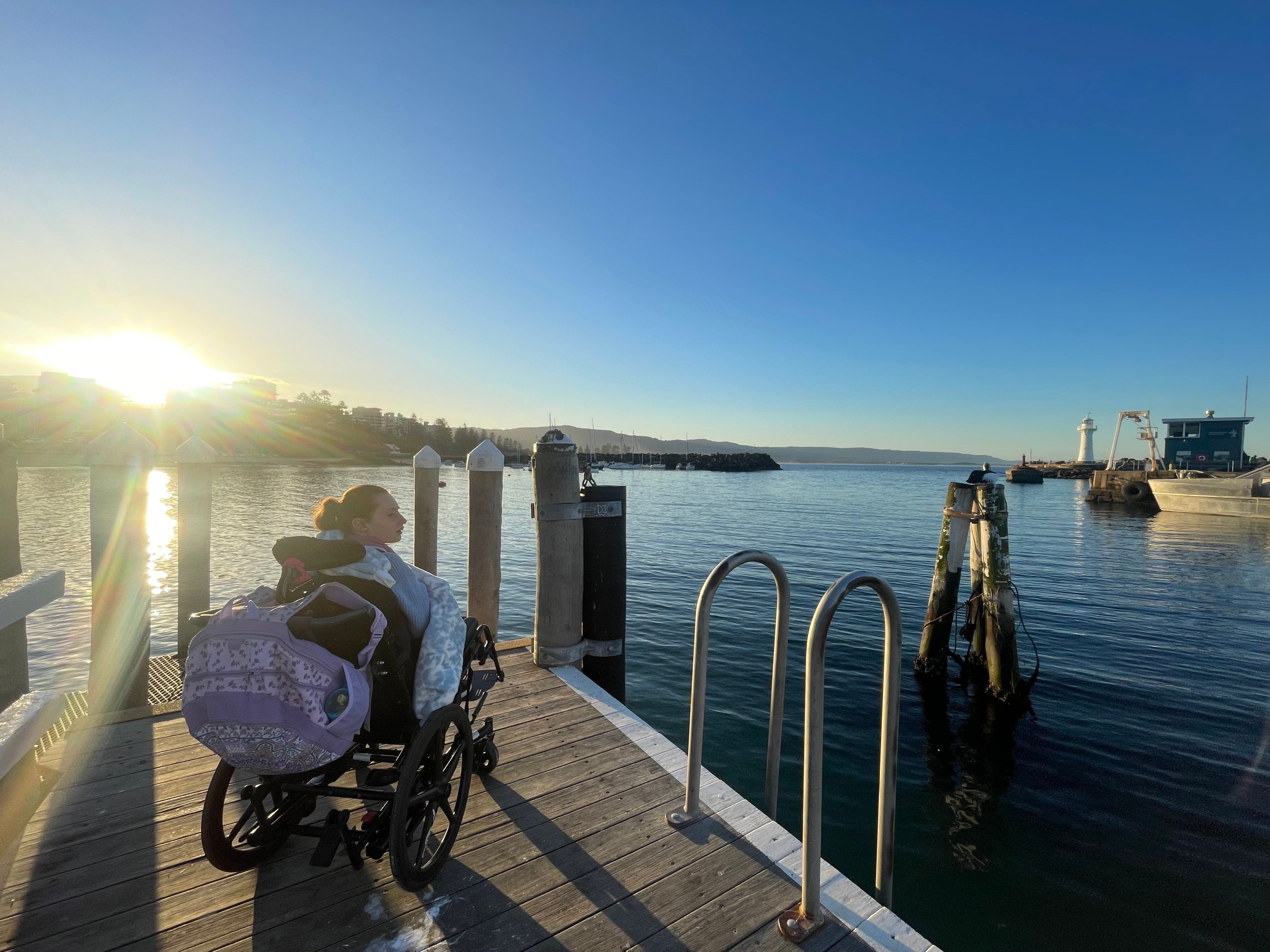 Picture of a young girl in a wheelchair, looking out over Wollongong Harbour at sunset